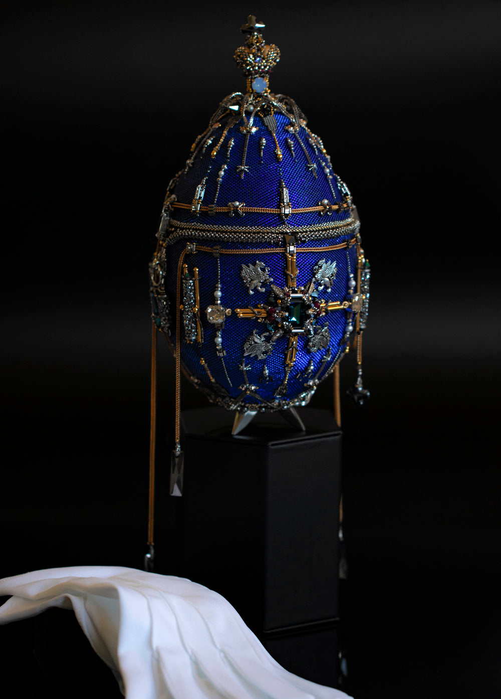 A blue and gold clutch with intricate designs and embellishments, displayed on a stand with a magnetic base.